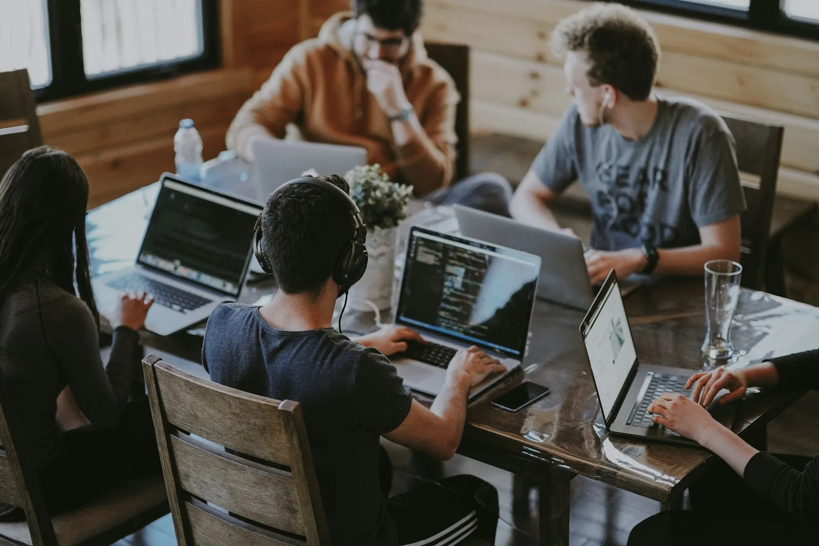 Lockere Beratungsrunde mit mehreren Laptops an einem Holztisch